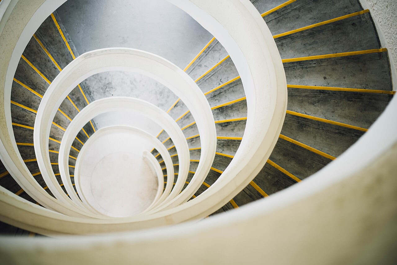 Looking down a spiral staircase, with repeating white curves and yellow-edged steps.