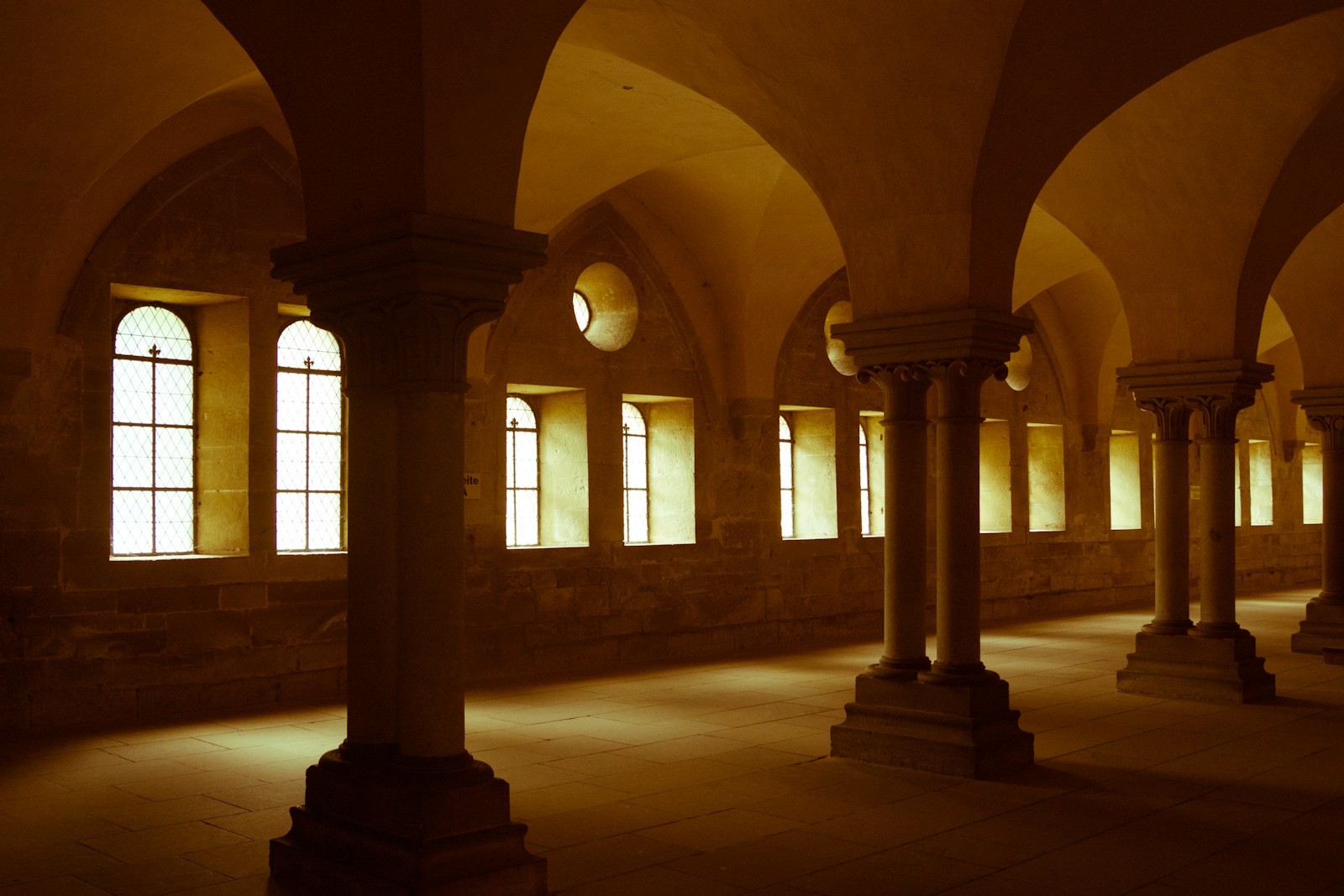 Warm sunlight falls through a row of stone arches and windows.